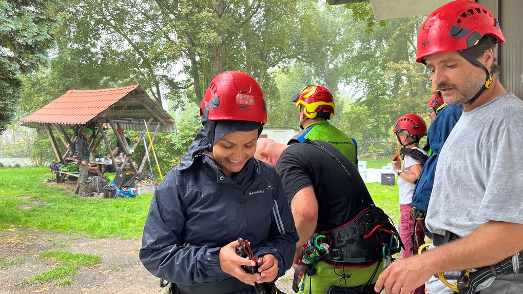 Members of the rope climbing technique course during a forced break, during a downpour, all people in harnesses and helmets.