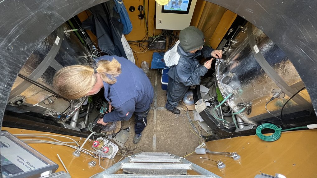 Inside a lysimeter of the company UGT in Majadas Spain. Two people repairing/maintaining the system. Two large insulated columns on the right and on the left in the picture above a formwork cabinet with visual button and at the bottom in the picture the ladder stairs. In between the orange plastic walls of the inner lining of the lysimeter cellar.